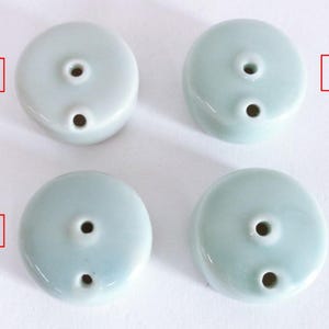 Puede incluir: Cuatro porta inciensos de cerámica azul pálido. Cada soporte es redondo con una parte superior plana y dos agujeros. Los soportes tienen un acabado brillante y están dispuestos en forma cuadrada. El color es un azul verdoso suave y apagado.