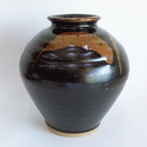 Pode incluir: Um vaso de cerâmica preto com um esmalte marrom. O vaso tem um corpo arredondado e um pescoço estreito.