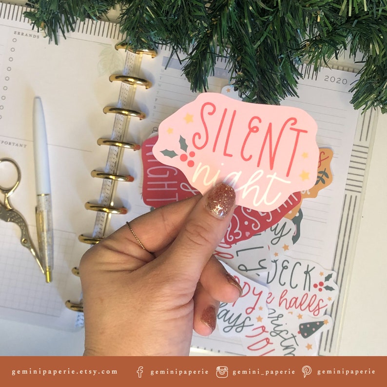 May include: A set of pink and red Christmas stickers with festive designs and text. The stickers feature phrases like "Silent Night", "Deck the Halls", and "Merry Christmas".