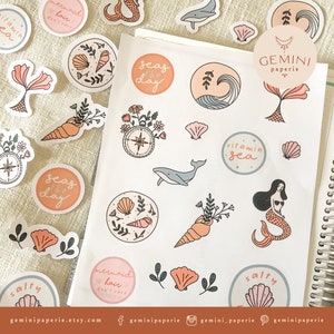 May include: A sheet of stickers with a sea theme. The stickers feature illustrations of seashells, mermaids, whales, and other ocean-related imagery. The stickers are in a variety of colors, including pink, blue, and green. The text "GEMINI paperie" is printed on one of the stickers.