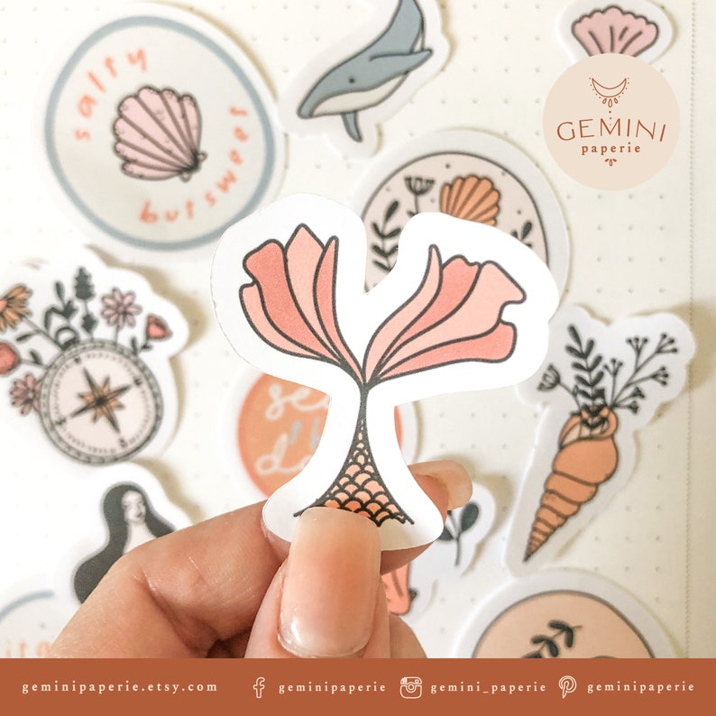 May include: A set of stickers featuring a variety of sea-themed illustrations, including a mermaid tail, a seashell, a compass, a whale, and a floral arrangement. The stickers are all white with pink and orange accents. The text "GEMINI paperie" is visible on one of the stickers.