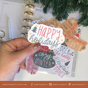 May include: A set of Christmas themed stickers with various designs, including "Happy holidays", "Cozy Winter", "Deck the halls", and "Christmas Addict".