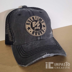 May include: A black and brown distressed trucker hat with a brown circle patch that says "Overtime BS pay Hours" in black lettering.