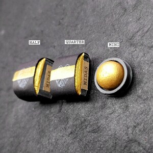 May include: Three different sizes of gold pigment in black containers labelled "Half", "Quarter", and "Mini" with the word "MIDAS" printed on the containers.