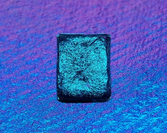 May include: A small, square, iridescent teal-colored tile with a textured surface.