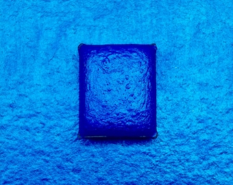 May include: A square, blue watercolor pan with a textured surface.