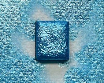 May include: A square pan of metallic blue watercolor paint. The paint has a shimmery, iridescent finish.