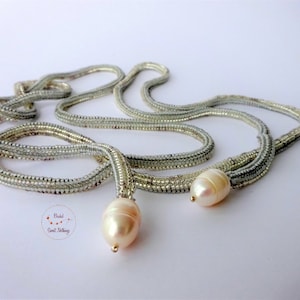May include: A long silver beaded necklace with two large white pearls at the ends.
