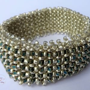 May include: A silver and blue beaded bracelet with a woven pattern. The bracelet is made with small, round beads and has a subtle ombre effect.