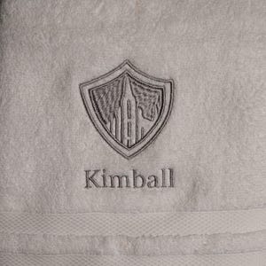May include: White towel with a gray embroidered shield design and the name Kimball.