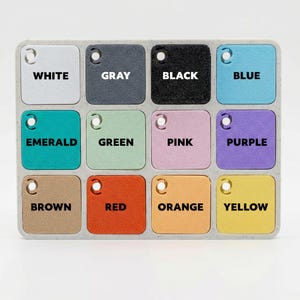 May include: A colour palette featuring twelve square colour swatches in a rectangular tray. Colours include white, grey, black, blue, emerald, green, pink, purple, brown, red, orange, and yellow. Each swatch has a hole and a colour name.