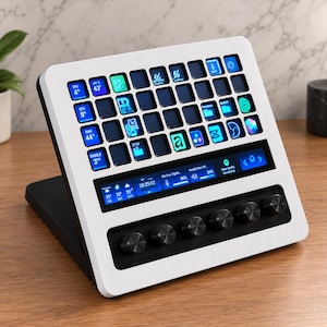 May include: A white and black macro keypad featuring a grid of backlit square keys with various digital icons, a horizontal status display screen showing system metrics and time, and six circular black control knobs along the bottom edge.