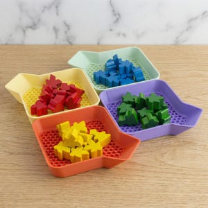May include: Four brightly coloured game piece trays, each holding wooden game pieces. The trays are yellow, orange, green, and purple, with a honeycomb base. The wooden pieces are red, yellow, blue, and green.