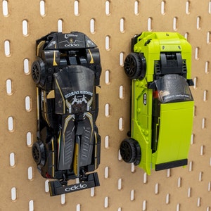 May include: Two toy sports cars, one black and gold, the other lime green, are mounted on a pegboard. The black car has "ROGER DUBUIS" and "oddo" printed on it. The green car has the number "8" printed on it.