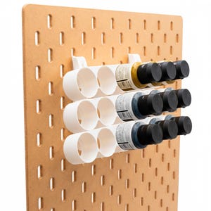 Peut inclure: Un panneau perforé en bois clair avec trois supports en plastique blanc. Chaque support est conçu pour contenir deux flacons. Les supports contiennent des flacons de différentes couleurs, avec des bouchons noirs.