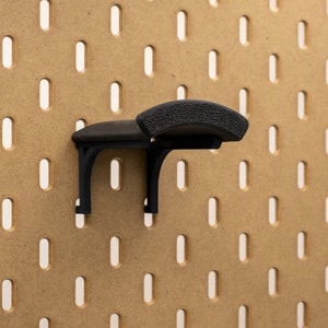 May include: A black pegboard hook with a textured, curved top. The hook is mounted on a brown pegboard with evenly spaced, vertical slots. The hook is designed to hold items on the pegboard.
