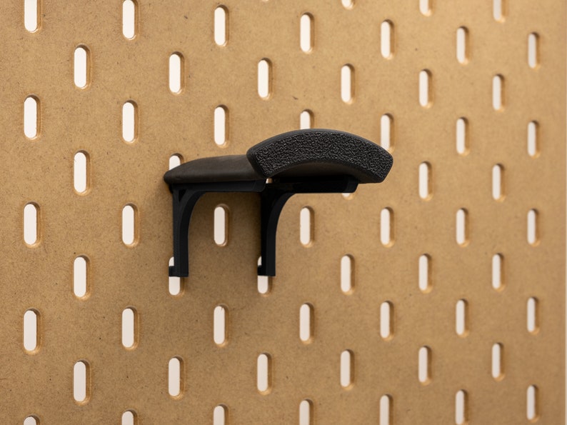 May include: A black pegboard hook with a textured, curved top. The hook is mounted on a brown pegboard with evenly spaced, vertical slots. The hook is designed to hold items on the pegboard.