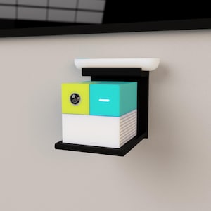 May include: A black wall-mounted shelf with a white top and a lower shelf. It holds three stacked, colorful boxes: a lime green and teal cube, and a white box with a dotted pattern. The boxes have a minimalist design.