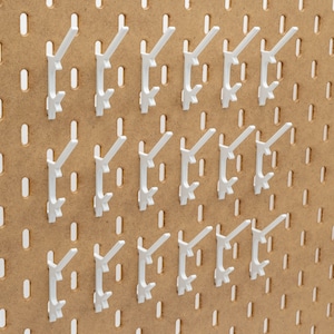 May include: A collection of white pegboard hooks arranged on a brown pegboard. The hooks are evenly spaced and designed to hold items. The pegboard has evenly spaced holes for hook placement, creating an organized storage solution.
