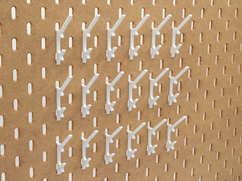 May include: A collection of white pegboard hooks arranged on a brown pegboard. The hooks are evenly spaced and designed to hold items. The pegboard has evenly spaced holes for hook placement, creating an organized storage solution.