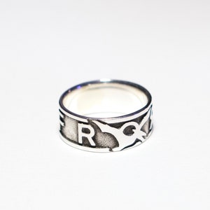 May include: A silver ring with a stylized design featuring a bird and the letter "R".