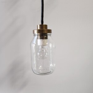 May include: A clear glass jar pendant light with a brass top and a black cord. The light bulb is visible inside the jar.