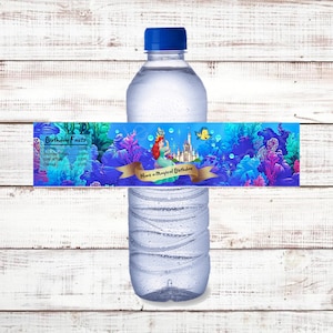 May include: Water bottle label with a mermaid and castle illustration. The label has a blue, purple, and green background with a gold ribbon that says "Have a Magical Birthday". The label also includes a list of birthday facts with a 100% rating for friends, birthday treats, lots of fun, and games.