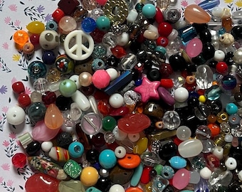 May include: A colorful assortment of beads in various shapes, sizes, and colors. The beads include round, teardrop, and star shapes, with colors like pink, blue, red, and clear. A white peace sign bead is also visible.
