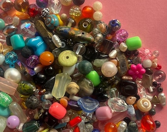 May include: A colorful assortment of beads in various shapes, sizes, and materials. The beads include glass, stone, and plastic in shades of blue, green, orange, pink, and brown. Some beads have intricate patterns and textures, perfect for jewelry making.