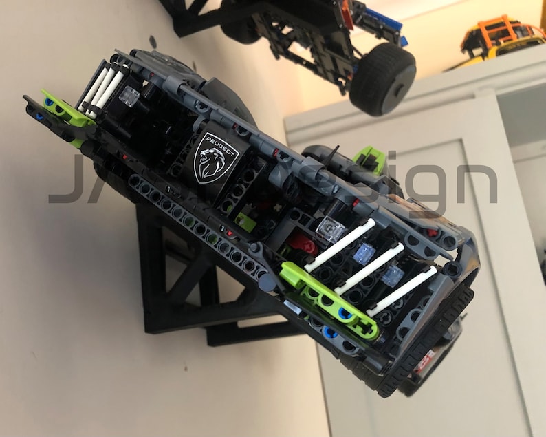 May include: A black and green Lego model car with a white Peugeot logo on the side. The car is mounted on a black wall mount.