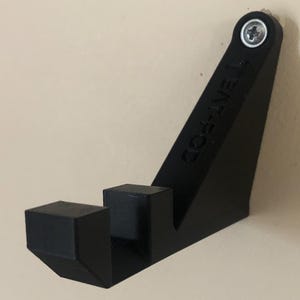 Op de afbeelding: Zwarte plastic wandbeugel met de tekst "GO-LIVE" erop gedrukt. De beugel heeft een schroefgat bovenaan en twee pinnen onderaan.