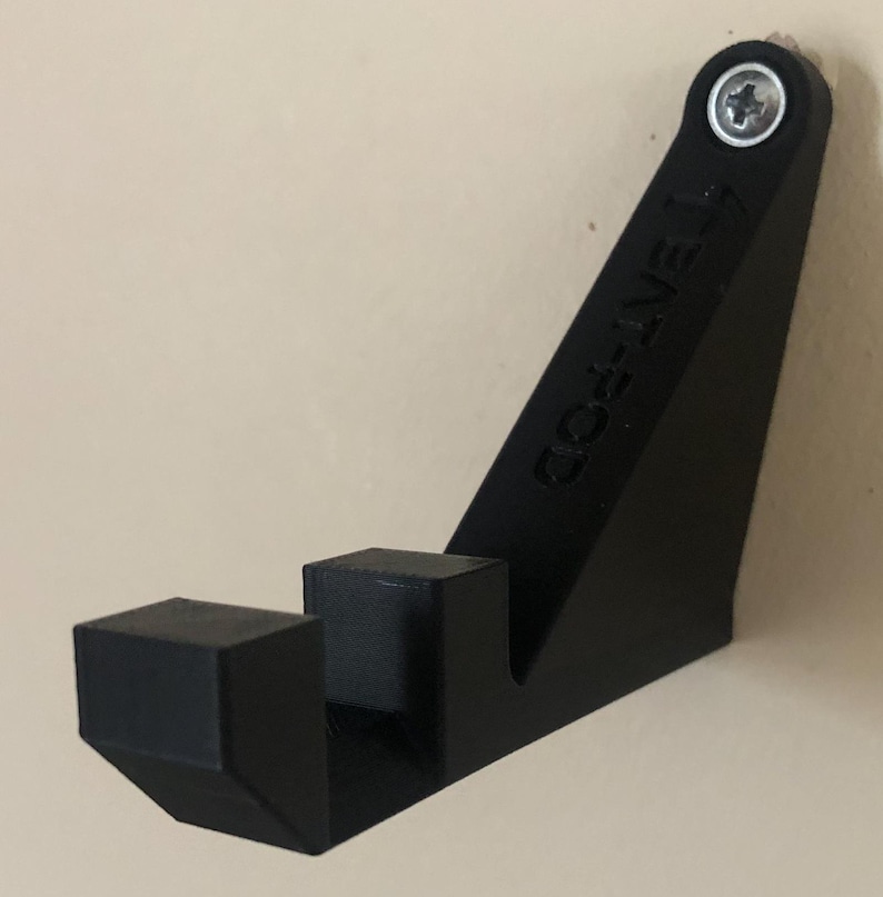 Op de afbeelding: Zwarte plastic wandbeugel met de tekst "GO-LIVE" erop gedrukt. De beugel heeft een schroefgat bovenaan en twee pinnen onderaan.