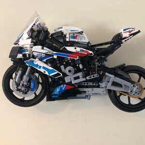 May include: A white, blue, and red LEGO&reg; Technic&trade; BMW M 1000 RR motorcycle model with a black frame and wheels. The motorcycle has a detailed engine and suspension system.