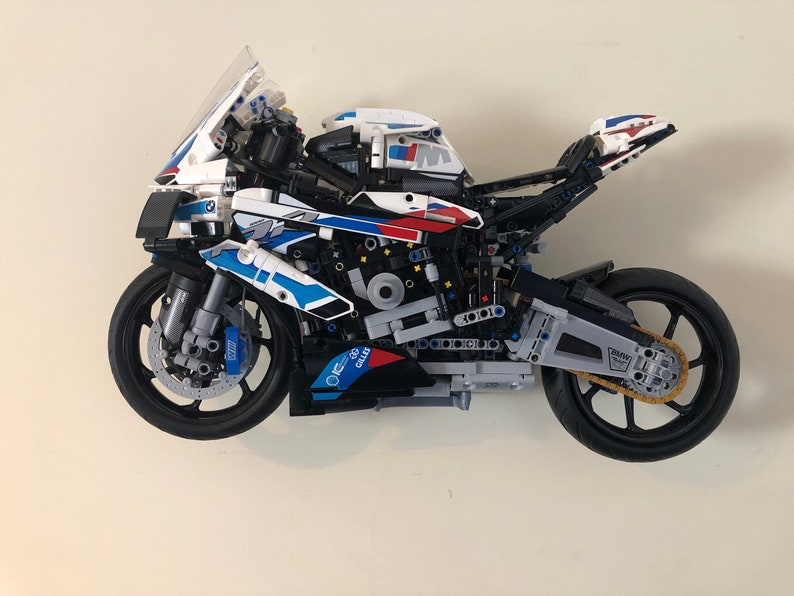May include: A white, blue, and red LEGO&reg; Technic&trade; BMW M 1000 RR motorcycle model with a black frame and wheels. The motorcycle has a detailed engine and suspension system.