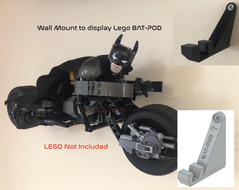 Op de afbeelding: Een zwarte plastic wandbeugel ontworpen om een Lego Bat-Pod te presenteren. De beugel heeft de vorm van een driehoek met een gebogen bovenkant en een kleine rand aan de onderkant. De beugel wordt getoond met een Lego Bat-Pod die eraan is bevestigd. De tekst "BAT-POD" is op de beugel gedrukt. De tekst "LEGO Not Included" is onder de beugel gedrukt.