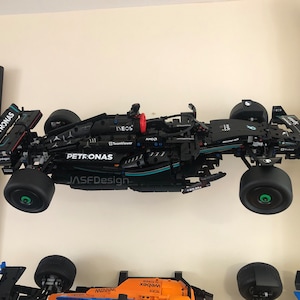 May include: A black LEGO model of a Formula 1 race car with the Petronas logo and the words "INEOS" and "TeamViewer" on the side. The car is mounted on a wall and has green wheels.