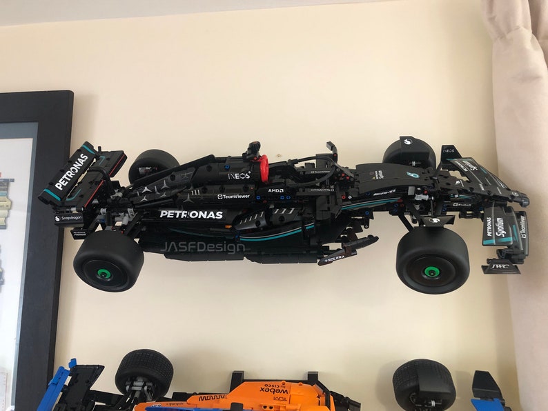 May include: A black LEGO model of a Formula 1 race car with the Petronas logo and the words "INEOS" and "TeamViewer" on the side. The car is mounted on a wall and has green wheels.