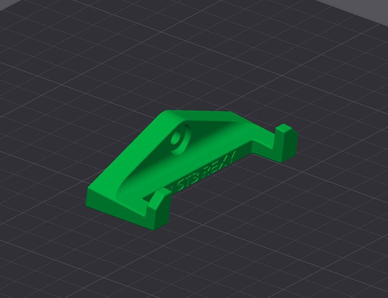 Op de afbeelding: Een heldergroen 3D-geprint object met een gebogen ontwerp, een cirkelvormig gat en een kleine rechthoekige uitsteeksel. De tekst "GTS REX" is zichtbaar aan de zijkant. Geplaatst tegen een donkergrijze rasterachtergrond.