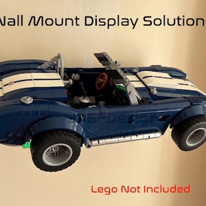 Op de afbeelding: Een blauwe speelgoedauto met witte racestrepen is aan de muur bevestigd. De auto heeft zwarte banden en een rood stuurwiel. De tekst "Wall Mount Display Solution" staat boven de auto.