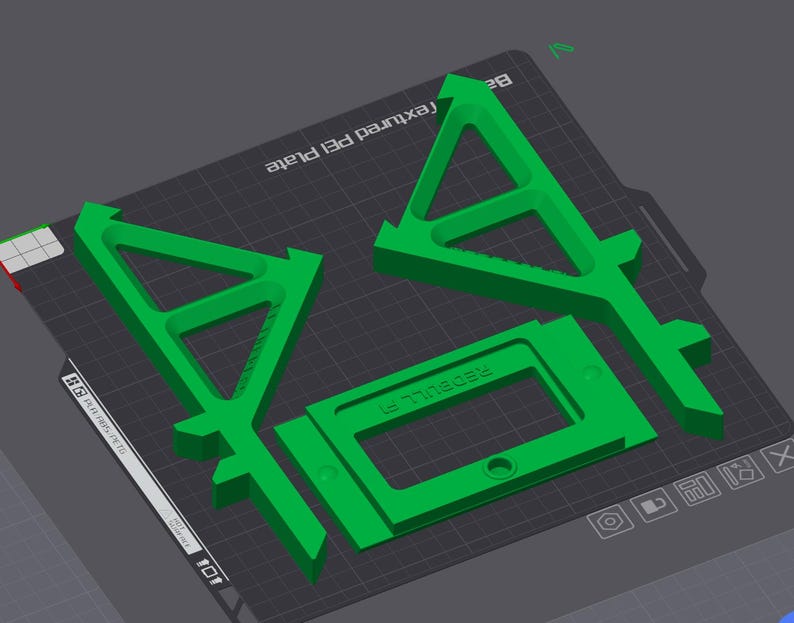 May include: Green 3D-printed parts, including two triangular shapes with arrow-like tops and a rectangular frame with the text "REDBULL F1". The parts are arranged on a textured surface.