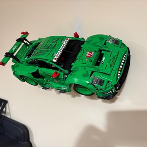 May include: A bright green toy sports car with black accents and a large rear wing. The car features the word "PORSCHE" in white and the number "77". The car has a detailed design with a unique front end.