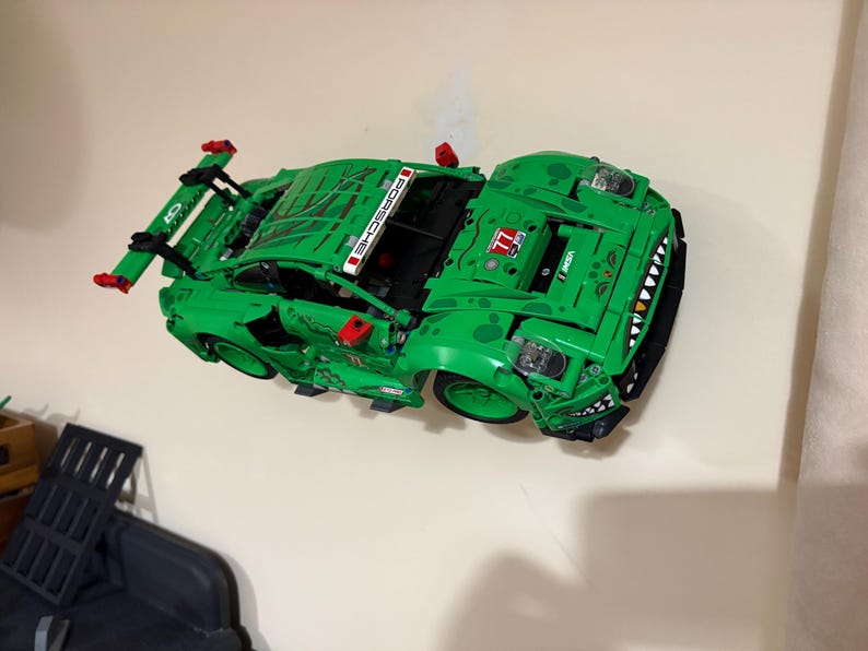 May include: A bright green toy sports car with black accents and a large rear wing. The car features the word "PORSCHE" in white and the number "77". The car has a detailed design with a unique front end.