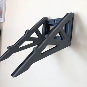 Puede incluir: Una estanter&iacute;a de pared negra con un dise&ntilde;o geom&eacute;trico. La estanter&iacute;a est&aacute; hecha de madera y tiene una forma triangular. Est&aacute; dise&ntilde;ada para sostener un port&aacute;til u otros dispositivos electr&oacute;nicos.