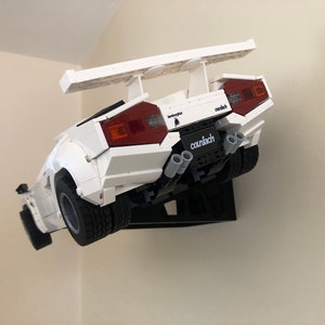 May include: A white Lego Lamborghini Countach model with a rear wing, red taillights, and the text "Lamborghini Countach" printed on the back.