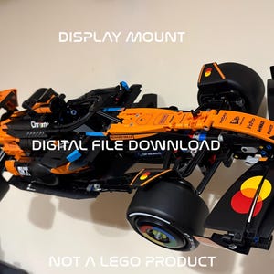 May include: An orange and black model race car is mounted on a wall. The model has the words "Chrome" and "McLaren" on it. The text "DISPLAY MOUNT", "DIGITAL FILE DOWNLOAD", and "NOT A LEGO PRODUCT" are also visible.