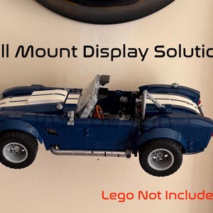 Op de afbeelding: Een blauwe en witte speelgoedauto is aan de muur bevestigd. De auto heeft een cabriokap en zilveren wielen. De tekst "Wall Mount Display Solution" staat boven de auto en "Lego Not Included" eronder.