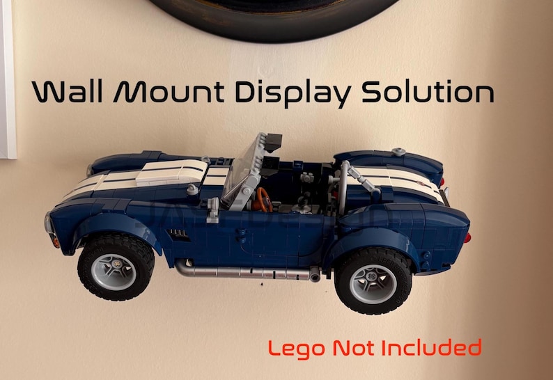 Op de afbeelding: Een blauwe en witte speelgoedauto is aan de muur bevestigd. De auto heeft een cabriokap en zilveren wielen. De tekst "Wall Mount Display Solution" staat boven de auto en "Lego Not Included" eronder.