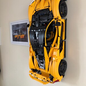 May include: A yellow Lego model of a sports car, with the engine and interior visible, is mounted on a wall.