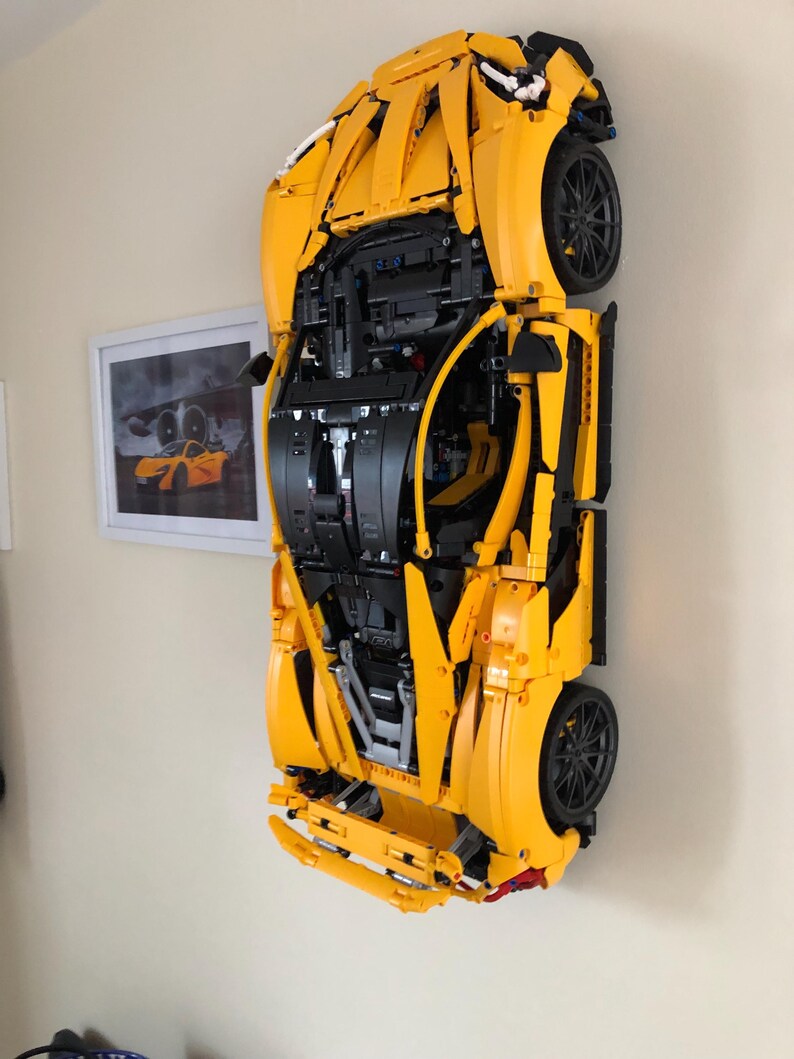 May include: A yellow Lego model of a sports car, with the engine and interior visible, is mounted on a wall.