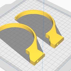May include: Two yellow, semi-circular objects with a flat base and a small hole. The objects are on a grid background, casting shadows. The design appears to be a 3D rendering or a digital model.